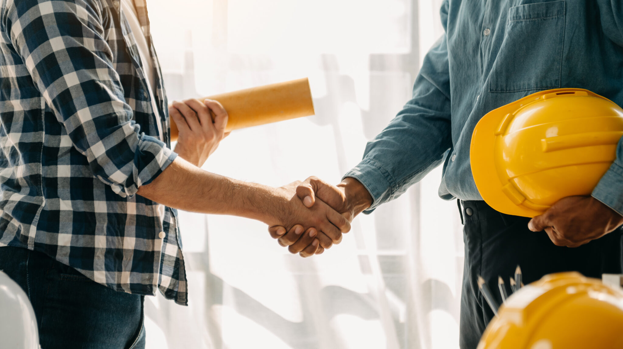 Construction team shake hands greeting start new project plan behind yellow helmet on desk in modern office center to consults about their building project.